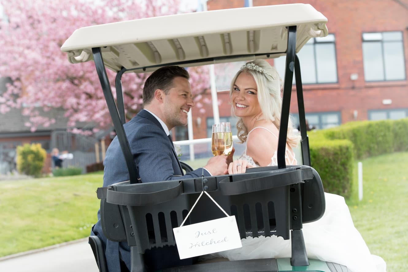 Couple celebrating their wedding with a glass of fizzy wine on a golf caddy
